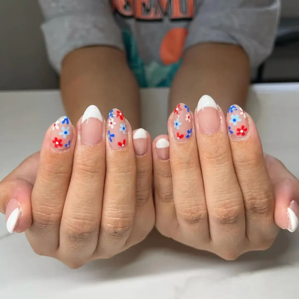 Patriotic French manicure with blue tips, a thin red line, and floral accents for an elegant 4th of July look